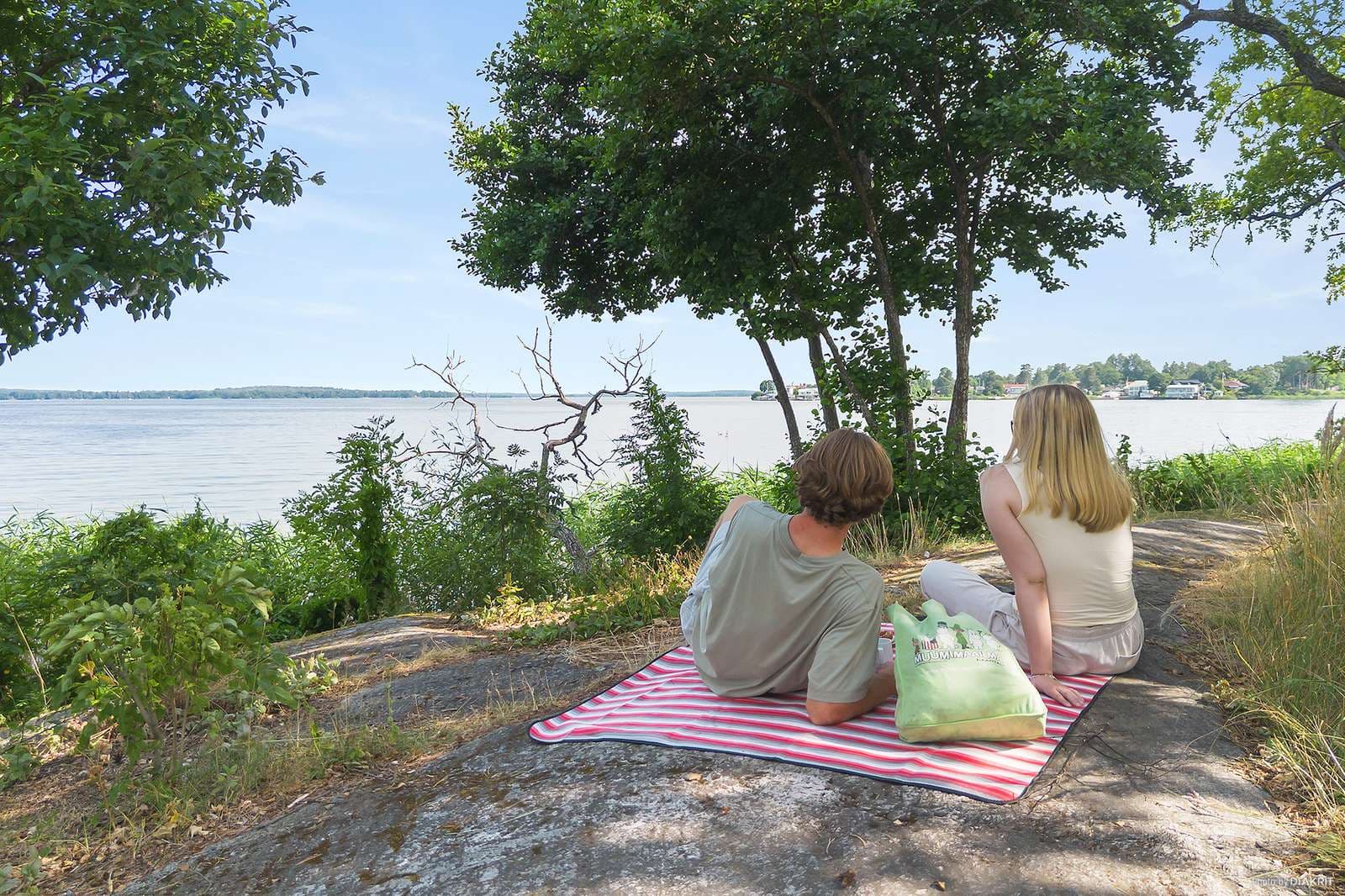 Västerås Mälaren påar som sitter vid strandkanten på en filt och tittar ut över vattnet.