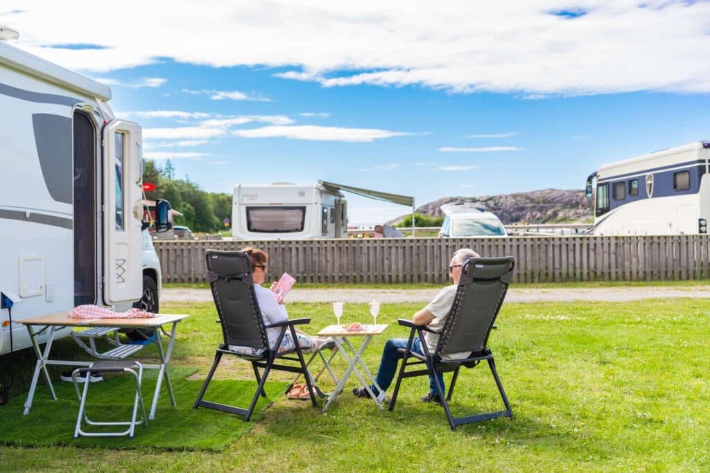 Campingstolar på en grön gräsmatta med husbilar och campingtomter i bakgrunden.